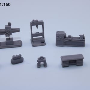 May include: A collection of miniature gray workshop tools, including a drill press, lathe, and workbench. The text "N-scale 1:160" is visible in the upper left corner. A logo is in the upper right corner.