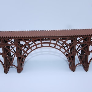 Puede incluir: Un puente modelo de madera marrón con un diseño arqueado. El puente tiene una estructura de celosía detallada y un techo de listones. El modelo está diseñado para exhibición o uso en un juego de trenes modelo.