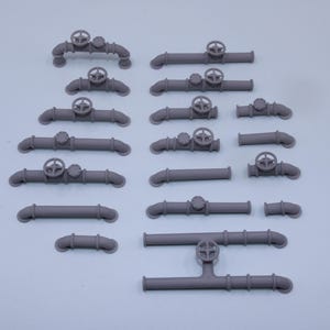 May include: A collection of grey miniature pipe components for model building, featuring various straight segments, elbow joints, and pipes equipped with circular hand wheels and valve caps, all arranged in a grid on a plain light background.