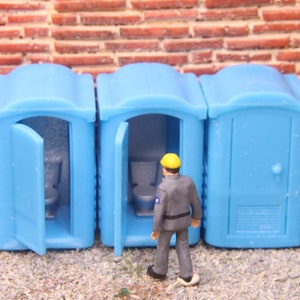 Puede incluir: Tres baños portátiles azules con una pequeña figura con un casco amarillo de pie frente al baño del medio.
