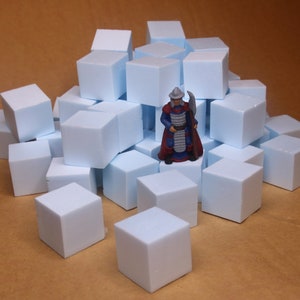 Könnte beinhalten: Eine Miniaturfigur eines Kriegers mit silbernem Helm, blauer Tunika und rotem Umhang, die auf einem großen Haufen hellblauer Schaumstoffwürfel steht. Der Krieger hält eine silberne Axt in der Hand und ist zentral zwischen den Blöcken platziert.