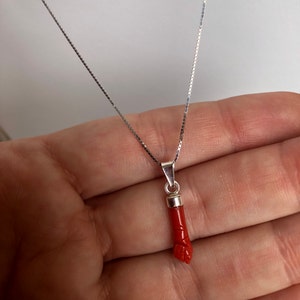 Könnte beinhalten: Eine silberne Kettenkette mit einem roten Korallenanhänger in Form einer Hand. Der Anhänger ist detailliert geschnitzt und hat eine silberne Öse.