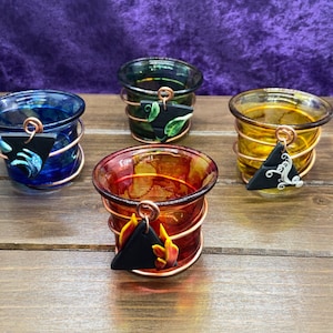 K&ouml;nnte beinhalten: Vier kleine Glas-Kerzenhalter mit Kupferdraht umwickelt. Jeder Halter hat einen schwarzen dreieckigen Anh&auml;nger mit einem anderen Design: ein Blatt, eine Welle, eine Flamme und ein Wirbel.