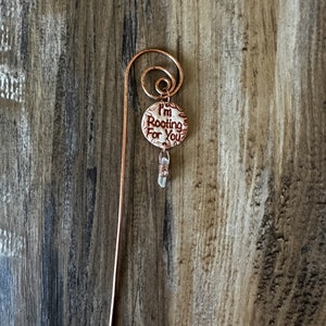 Puede incluir: Un marcap&aacute;ginas de cobre con un amuleto de cer&aacute;mica blanca que dice "Te estoy animando". Un cristal transparente cuelga del amuleto.