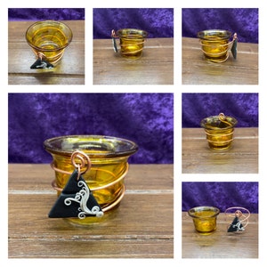 K&ouml;nnte beinhalten: Ein Satz mit f&uuml;nf Kerzenhaltern aus bernsteinfarbenem Glas, die oben mit Kupferdraht umwickelt sind. Jeder Halter hat einen schwarzen Dreiecksanh&auml;nger mit einem wei&szlig;en Wirbelmuster, der am Draht h&auml;ngt.