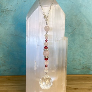 May include: A crystal suncatcher with a clear crystal ball at the bottom and a chain with pink and red beads.