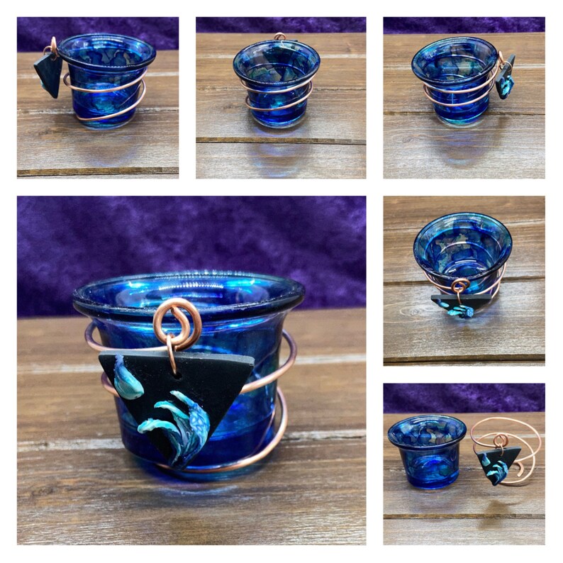 K&ouml;nnte beinhalten: Ein blauer Glas-Votivkerzenhalter mit einer Kupferdrahtumwicklung und einem schwarzen Dreiecksanh&auml;nger mit einem blauen Wellendesign.