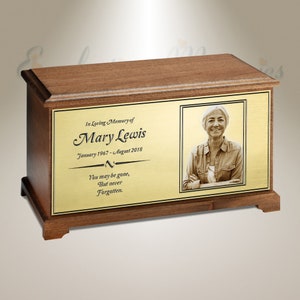 Pode incluir: Uma urna de cremação de madeira com uma placa dourada que apresenta uma foto de uma mulher e a inscrição "In Loving Memory of Mary Lewis Janeiro 1967 - Agosto 2018 Você pode ter partido, Mas nunca será esquecida."