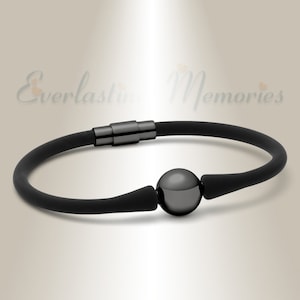 Può includere: Un braccialetto nero con chiusura magnetica e una sfera centrale. Il braccialetto è realizzato in un materiale scuro e flessibile e presenta un design minimalista. Il testo "Everlasting Memories" è sullo sfondo.