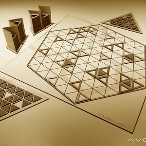 Puede incluir: Un juego de mesa de madera llamado "Ambush" con un área de juego hexagonal y piezas triangulares. El juego está hecho de madera marrón claro y tiene un diseño simple.