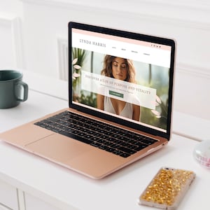 Pode incluir: Um computador port&aacute;til com um exterior rosa e dourado est&aacute; aberto para um site com o texto "LYNDA HARRIS" e "DISCOVER A LIFE OF PURPOSE AND VITALITY". O site apresenta uma foto de uma mulher com cabelo castanho comprido e uma blusa branca.