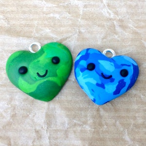 May include: Two small heart-shaped charms with a happy face. One charm is green with blue swirls and the other is blue with purple swirls.
