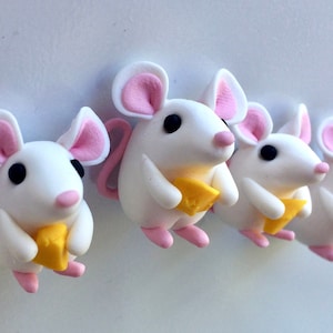 May include: Five white mice figurines with pink ears and tails, each holding a small yellow piece of cheese. The mice are arranged in a row on a white background.