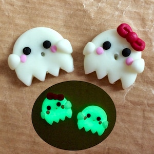 May include: Four small ghost-shaped ornaments, two white with black eyes and pink cheeks, one with a red bow, and two green that glow in the dark.