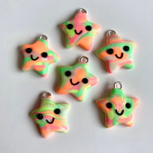May include: Six star-shaped charms in vibrant colours with a smiley face. The charms are a mix of orange, green, and pink, with a silver loop at the top. Ideal for jewellery making or other craft projects.