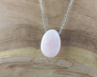 May include: A light pink oval-shaped pendant necklace. The pendant is made of a smooth, polished stone and is suspended from a delicate silver chain. The necklace is displayed against a wooden background.