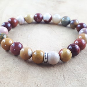 Könnte beinhalten: Ein Armband mit braunen, roten und weißen Perlen. Das Armband hat einen silbernen Akzent.