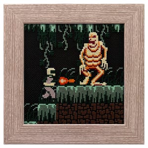 May include: Cross-stitch artwork in a wooden frame. The artwork depicts a pixelated skeleton figure in a dark, green-toned environment. The skeleton is tan and orange, with a pixelated design. The frame is a light brown color.