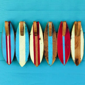 May include: Six wooden surfboard-shaped wall decorations with red, white, and blue stripes. The surfboards are hanging on a blue wall.