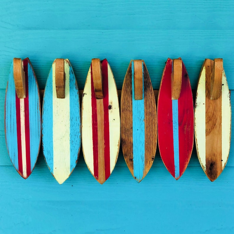 May include: Six wooden surfboard-shaped wall decorations with red, white, and blue stripes. The surfboards are hanging on a blue wall.