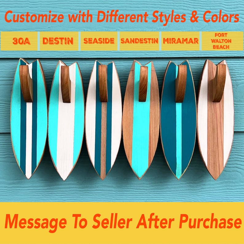 May include: Six wooden surfboard-shaped wall hooks in different color combinations. The hooks are painted with teal, white, and turquoise stripes. The text "30A DESTIN SEASIDE SANDESTIN MIRAMAR FORT WALTON BEACH" is printed on the top of the image.