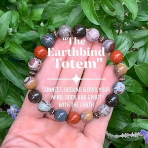 May include: A beaded bracelet featuring round, multi-colored stone beads in shades of red, brown, grey, and tan, interspersed with small, textured copper-toned metal spacers. The text "The Earthbind Totem" and "CONNECT, GROUND & BIND YOUR MIND, BODY AND SPIRIT WITH THE EARTH" is overlaid on the image.
