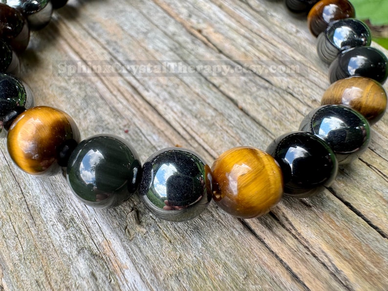 May include: A beaded bracelet featuring alternating polished spherical beads in tiger's eye with golden-brown chatoyancy and smooth, reflective black obsidian. The beads are strung together in a circular pattern, displaying a high-gloss finish.