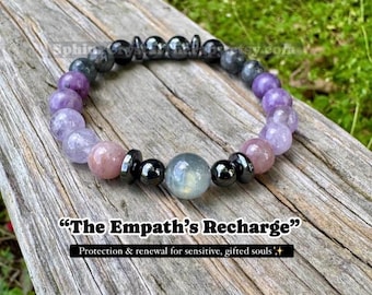 May include: A beaded bracelet featuring round purple, pink, and grey stones interspersed with small black metallic discs. The text "The Empath's Recharge" and "Protection & renewal for sensitive, gifted souls" is printed below the bracelet.