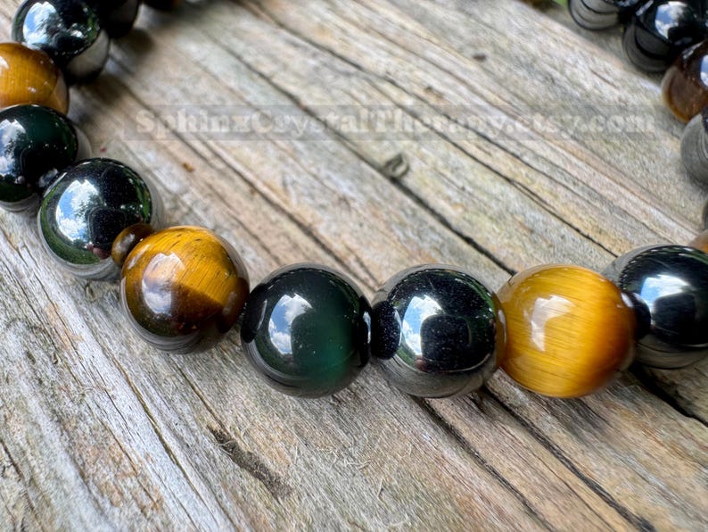 May include: A beaded bracelet featuring alternating polished spherical beads in golden-brown tiger eye, dark metallic hematite, and deep green obsidian. The beads are strung together in a repeating pattern, showcasing natural stone textures and reflective surfaces.