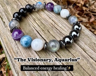 May include: A beaded bracelet featuring a mix of polished round stones in shades of black, purple, blue, white, and grey, accented with small metallic spacers. The text "The Visionary, Aquarius" and "Balanced energy healing" appears below.