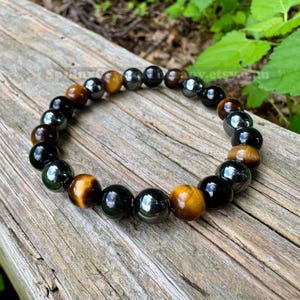May include: A beaded bracelet featuring alternating round polished beads in glossy black and golden-brown tiger eye. The beads are strung together in a circular pattern, showcasing a smooth, reflective surface on each individual stone bead.