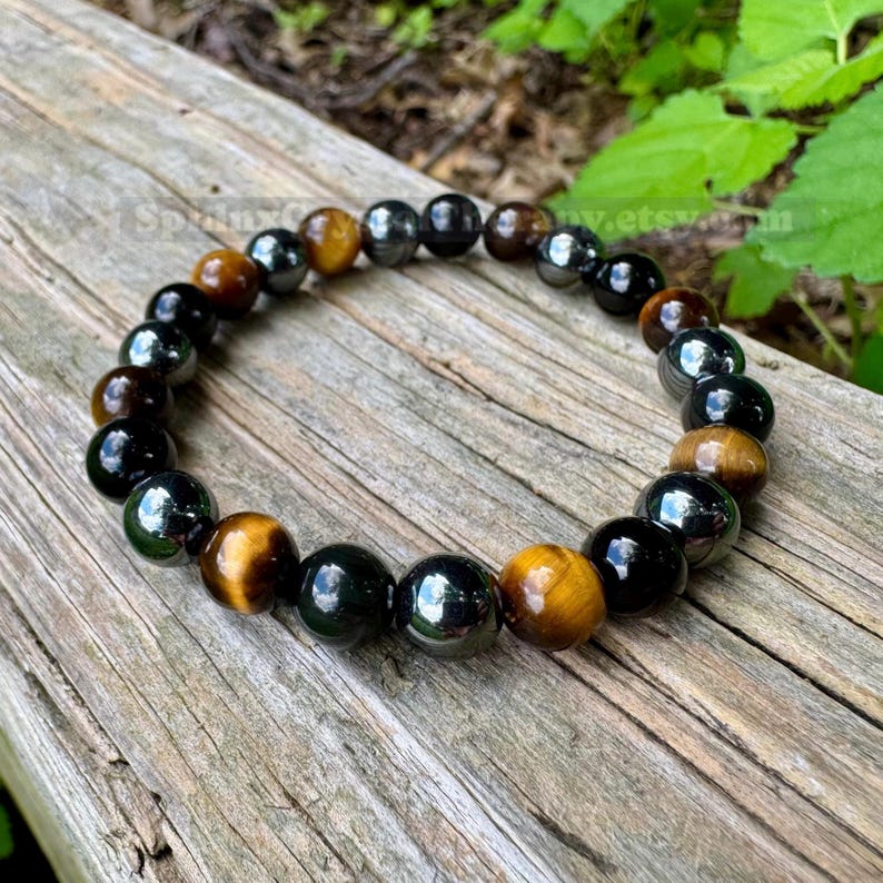 May include: A beaded bracelet featuring alternating round polished beads in glossy black and golden-brown tiger eye. The beads are strung together in a circular pattern, showcasing a smooth, reflective surface on each individual stone bead.