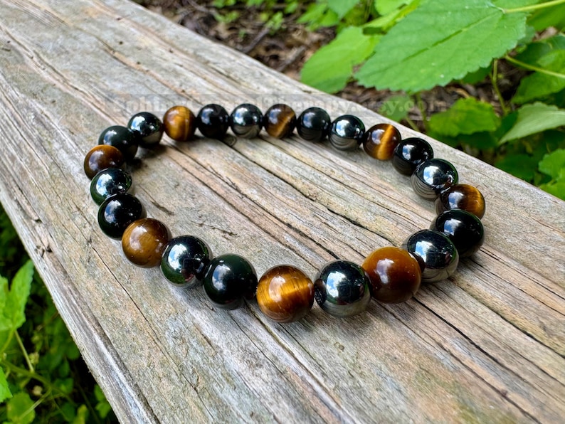 May include: A beaded bracelet featuring alternating polished round beads in shades of golden brown tiger eye and glossy black obsidian. The beads are strung together in a circular pattern, showcasing a smooth, reflective surface on each individual stone.