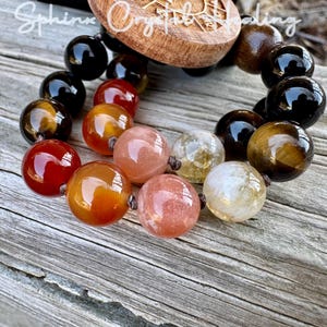 Puede incluir: Un brazalete de cuentas con cuentas negras, ojo de tigre, cornalina, piedra de sol y cuarzo transparente. El brazalete est&aacute; atado con un cord&oacute;n marr&oacute;n y tiene un dije de madera con las palabras "Sphinx Crystal Healing".