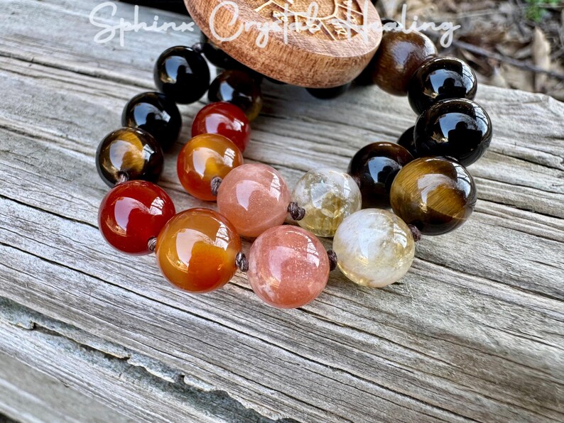 Puede incluir: Un brazalete de cuentas con cuentas negras, ojo de tigre, cornalina, piedra de sol y cuarzo transparente. El brazalete est&aacute; atado con un cord&oacute;n marr&oacute;n y tiene un dije de madera con las palabras "Sphinx Crystal Healing".