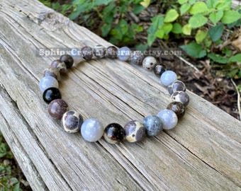 May include: A beaded bracelet featuring round polished stones in shades of light blue, dark brown, cream, and grey. The beads are arranged in a circular pattern. The text SphinxCrystatherapy.etsy.com is visible across the center of the image.