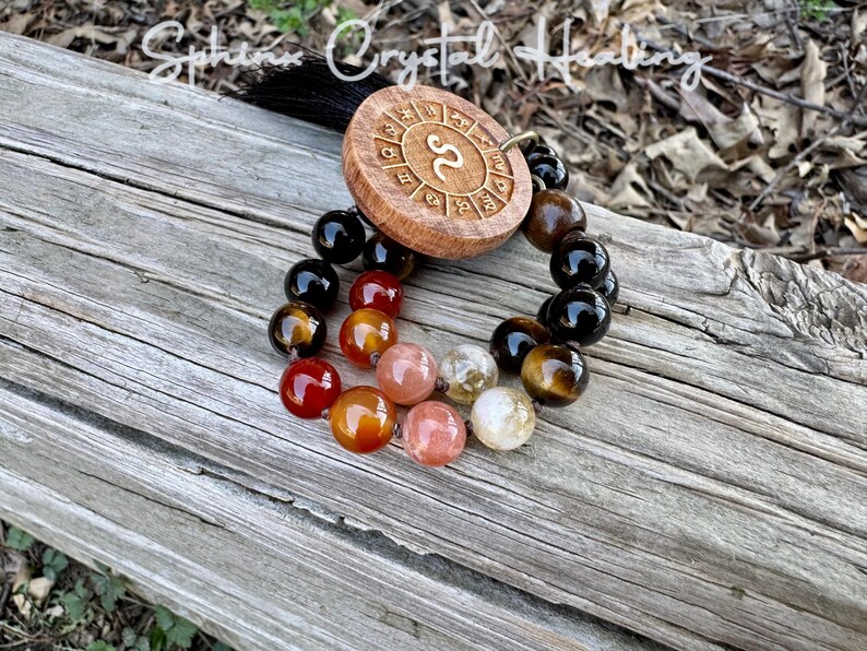 Puede incluir: Un amuleto de madera del zod&iacute;aco con el s&iacute;mbolo de Escorpio, rodeado de un brazalete de cuentas negras, marrones, naranjas y rojas.
