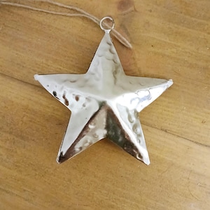 May include: A silver metal star ornament with a hammered texture. The star has a loop at the top for hanging.