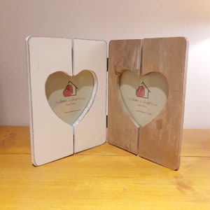 May include: A white and brown wooden picture frame with two heart-shaped openings. The frame has the text "The Home & Hearts Shop Home Decor" printed on it.