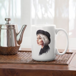 May include: White ceramic mug with a black and white illustration of a person wearing a black beret and a black jacket. The person has short, white hair and is looking to the side.