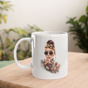 May include: White ceramic mug with a colorful illustration of a woman wearing sunglasses and a bandana. The woman has tattoos on her arms and is holding a cup.