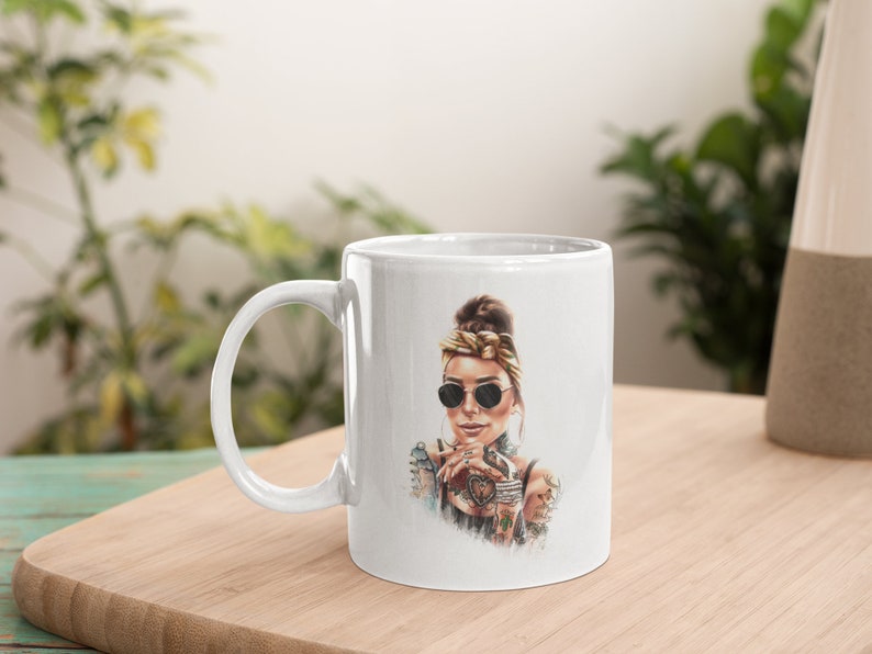May include: White ceramic mug with a colorful illustration of a woman wearing sunglasses and a bandana. The woman has tattoos on her arms and is holding a cup.