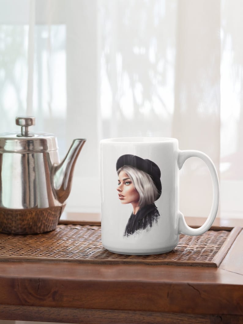 May include: White ceramic mug with a black and white illustration of a person wearing a black beret and a black jacket. The person has short, white hair and is looking to the side.
