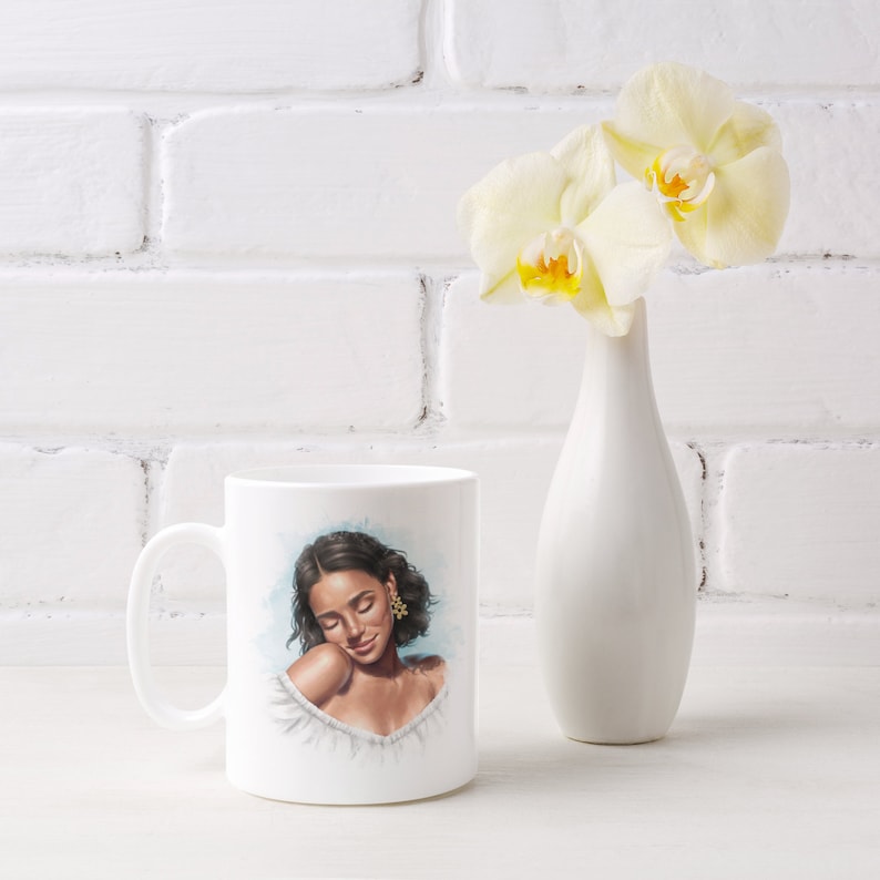 May include: White ceramic mug with a colorful illustration of a woman with brown hair and eyes, wearing a white top and gold earrings. The mug is on a white surface with a white vase and yellow flowers in the background.