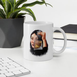May include: White ceramic mug with a colorful illustration of a person holding a plastic bag with goldfish inside. The person's face is partially obscured by the bag.