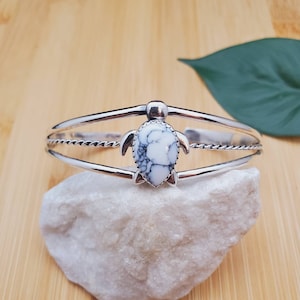 May include: A silver bracelet with a white and black turtle charm. The bracelet has a twisted rope design and is made of sterling silver.