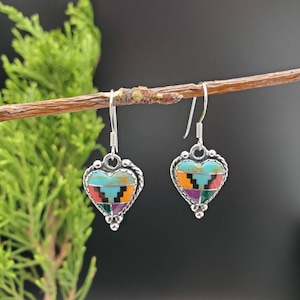 May include: A pair of silver heart-shaped earrings with a colorful geometric pattern made of turquoise, orange, red, purple, and green stones.