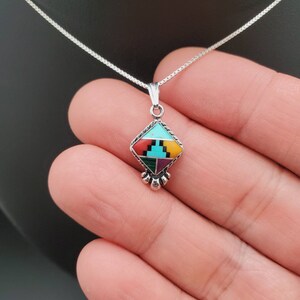 May include: A silver necklace with a diamond-shaped pendant featuring a colorful inlay of turquoise, red, yellow, and green stones.