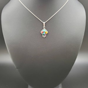 May include: A silver chain necklace with a small, square pendant featuring a geometric design of turquoise, red, yellow, green, and black stones.