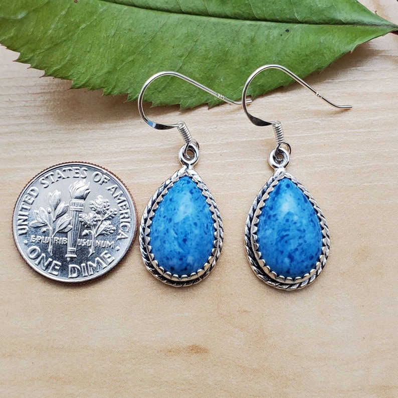 May include: A pair of silver dangle earrings with blue gemstone teardrop shaped drops. The earrings are about the size of a dime.
